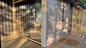 A modern outdoor shower area with a wooden deck, a glass door, and a metal showerhead. - The Villa – Lake Escape w/ Sauna, Jacuzzi & Boats (Vegby)