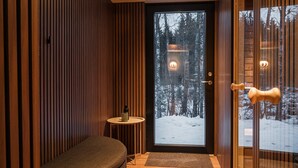 A modern interior with a wooden slat wall, a round table with a candle, and a door leading to a snowy outdoor area. - The Villa – Lake Escape w/ Sauna, Jacuzzi & Boats (Vegby)