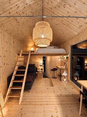 Een knus houten interieur met een slaapverdieping, een trap, een bank, een eettafel en een hanglamp.