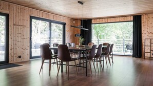 A modern dining area with a wooden ceiling, large windows, and a round table surrounded by chairs. - Ladhus One - Fancy Nature Hill home by the lake (Floda)