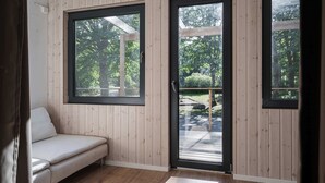 A room with wooden walls, a bench, and large windows with a view of a deck and trees. - Ladhus One - Fancy Nature Hill home by the lake (Floda)