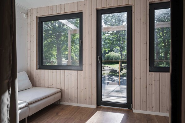 A room with wooden walls, a bench, and large windows with a view of a deck and trees. - Ladhus One - Fancy Nature Hill home by the lake (Floda)