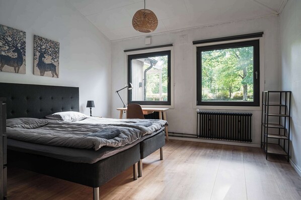Una camera da letto con un letto, una scrivania, una sedia, un termosifone e due finestre.