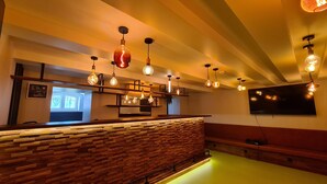 A bar area with wooden slats, hanging Edison bulbs, and a mounted TV. - Banana's Camp - Hostel (Cannes)