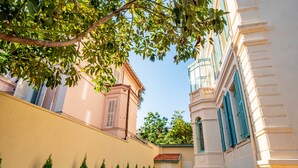 A courtyard with a building, a tree, and a row of coniferous trees. - Banana's Camp - Hostel (Cannes)