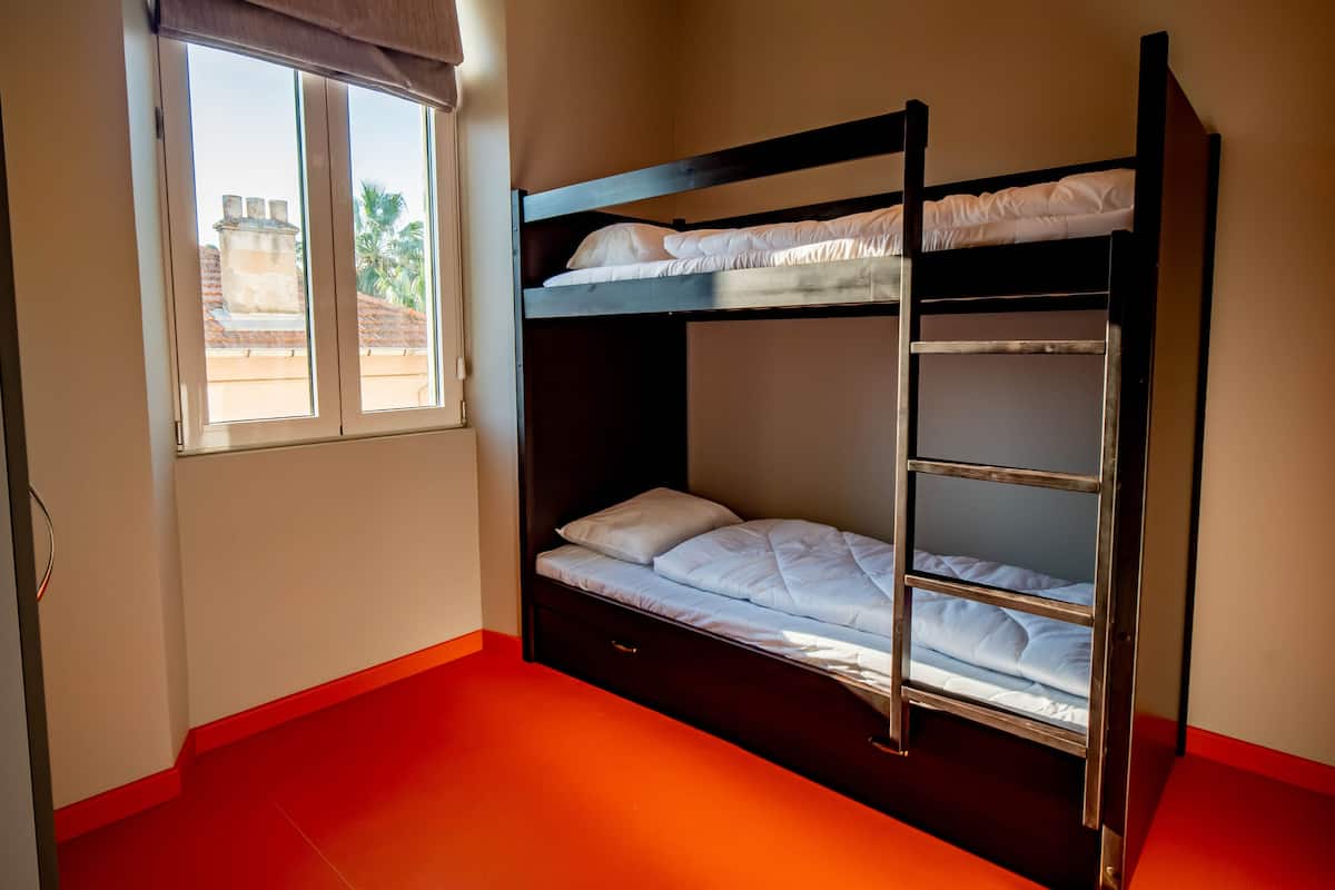 A bunk bed room with a window, red flooring, and a view of buildings outside.