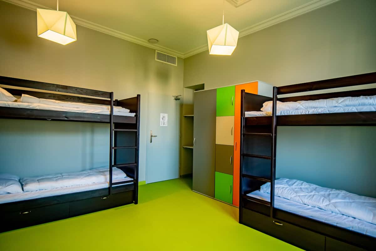 A dormitory room with bunk beds, a wardrobe, and a door.