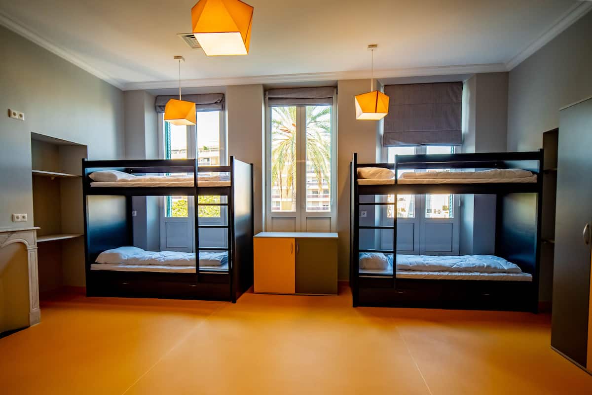 A dormitory room with bunk beds, a desk, and two pendant lights.