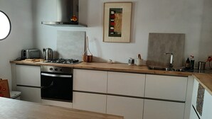 A modern kitchen with a gas stove, oven, and a stainless steel sink. There is a wooden countertop, a hanging light fixture, and a framed picture on the wall. - House in a typical hamlet - Cabo de Gata Park (Carboneras)