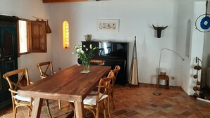 A dining area with a wooden table and chairs, a piano, and a wall-mounted TV. - House in a typical hamlet - Cabo de Gata Park (Carboneras)