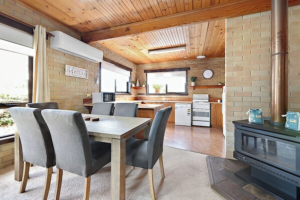 A modern kitchen with a brick wall, wooden ceiling, and a dining area with grey chairs and a wooden table. - Hook, Wine & Sinker Retreat (Stieglitz)
