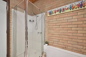 A glass-enclosed shower with a white bathtub and a decorative wall tile above it. - Hook, Wine & Sinker Retreat (Stieglitz)