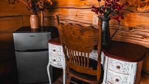 A rustic wooden interior with a wooden chair, a small table, and a vintage refrigerator. - Glamping Cabin | Huge Window | Over a Creek (Green Township)