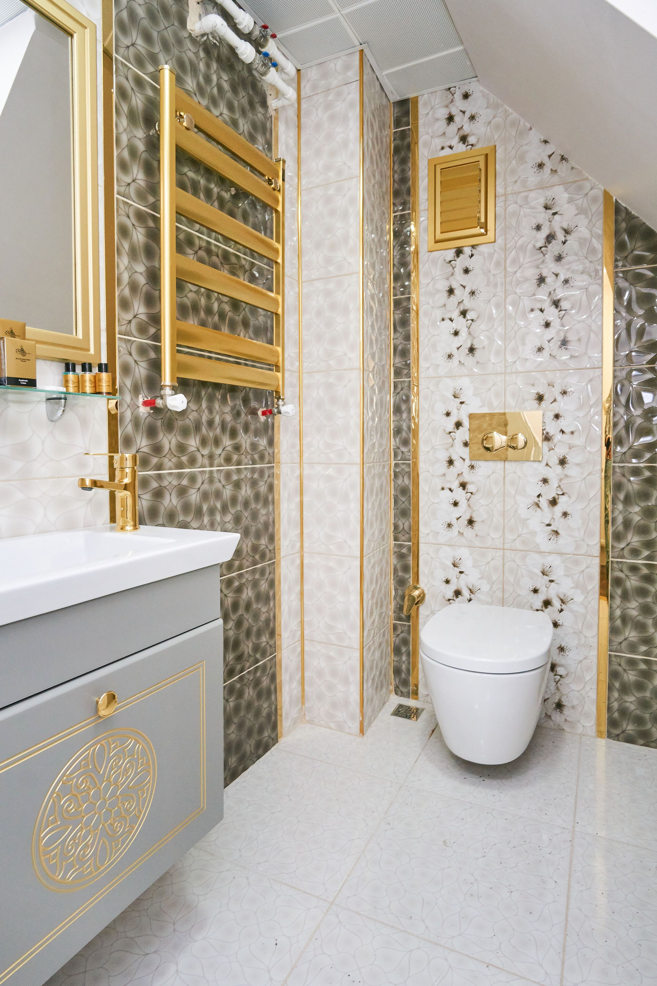 A bathroom with a white sink, gold fixtures, and patterned tiles.