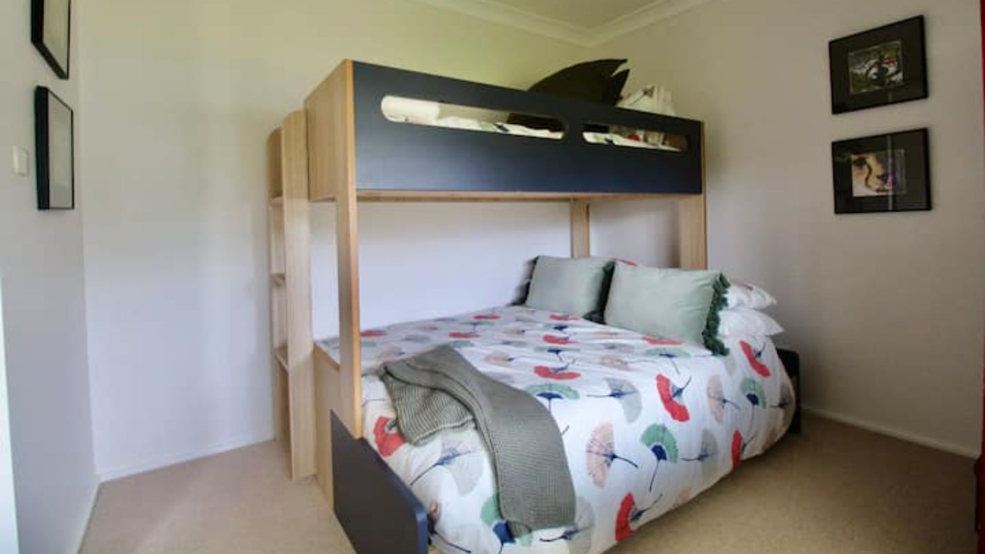 Una cama litera con un edredón y almohadas estampadas con motivos florales, un cabecero de madera y un pequeño estante en la parte superior.