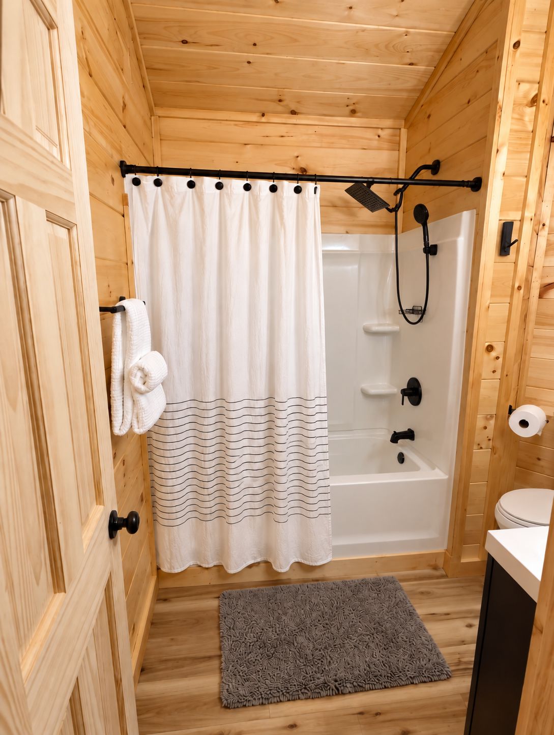 A wooden cabin bathroom with a shower, toilet, and a towel rack.