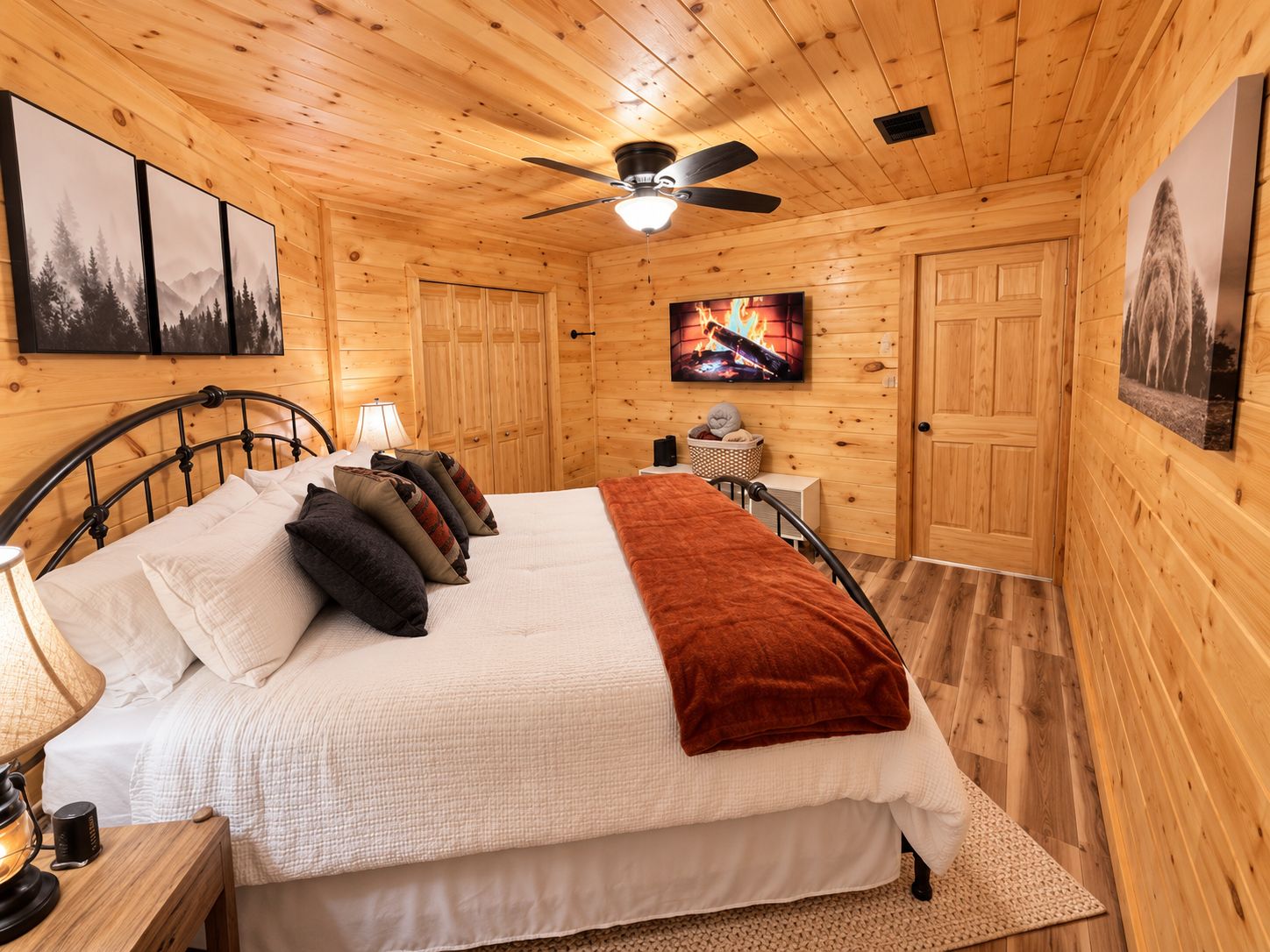 A wooden cabin bedroom with a bed, a ceiling fan, a television, and framed pictures on the walls.