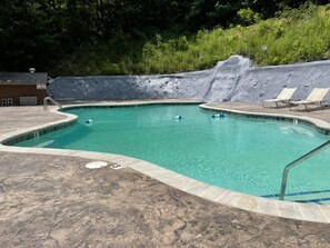 A swimming pool with a waterfall feature, lounge chairs, and a paved deck.