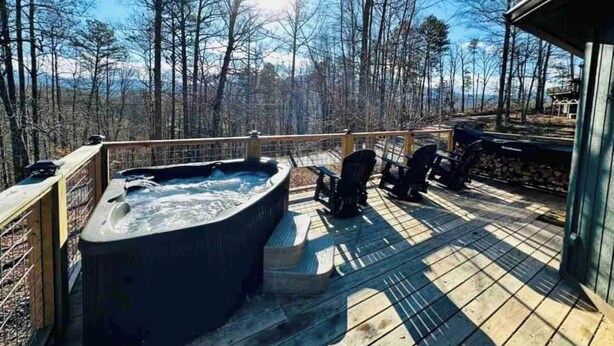 Ein Whirlpool auf einer Holzterrasse mit Blick auf einen Wald und Berge im Hintergrund.
