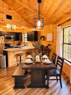 Interior de una cabaña de madera con cocina, comedor y un ventanal grande.
