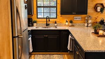A kitchen with wooden cabinets, a stainless steel refrigerator, a granite countertop, and a window with a view of greenery.