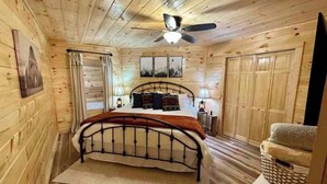 Ein Schlafzimmer einer Holzhütte mit einem Bett, einem Deckenventilator und einem Nachttisch.