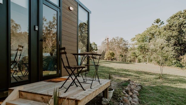 A modern building with a wooden deck, outdoor seating, and a view of a grassy area with trees. - Nomad Nation by Tiny Away (Mount Perry)