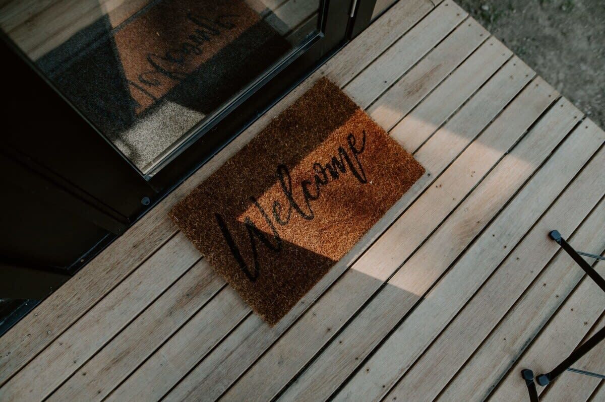 A wooden deck with a brown doormat that reads 'Welcome.'