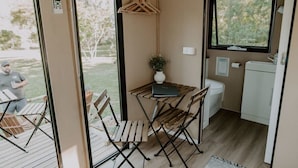 A compact living space with a foldable table, chairs, a small white sink, and a window. - Nomad Nation by Tiny Away (Mount Perry)