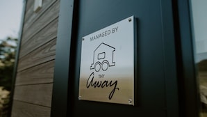 A sign with a house and truck icon, indicating management by Tiny Away. - Nomad Nation by Tiny Away (Mount Perry)