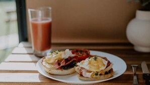 A breakfast plate with eggs Benedict and a glass of smoothie on a wooden table. - Nomad Nation by Tiny Away (Mount Perry)