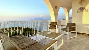 Un balcon offrant une vue sur la mer et les montagnes, aménagé avec un canapé, des fauteuils et une table.