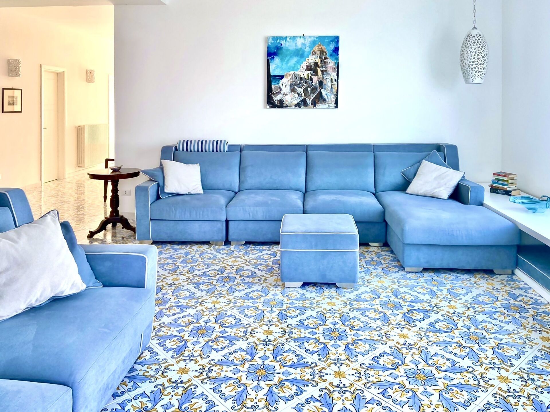 A living room with a blue sofa, matching ottoman, and patterned floor tiles.