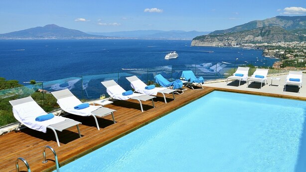 Un espace aménagé au bord de la piscine, avec des chaises longues et une vue sur la mer et les montagnes.
