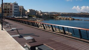 A wooden boardwalk with a metal railing, overlooking a body of water and buildings in the background. - Studio - Sleeps 2 - Balcony - 5 Min Walk To Beach (St. Paul's Bay)