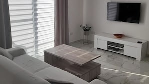 A modern living room with a sofa, a wooden coffee table, a white TV stand, and a floor with marble tiles. - Studio - Sleeps 2 - Balcony - 5 Min Walk To Beach (St. Paul's Bay)