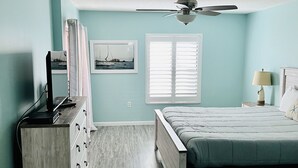 Un dormitorio con cama, cómoda, ventilador de techo y ventana con persianas.