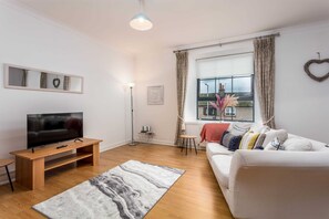 A modern living room with a flat-screen TV, a white sofa, a wooden coffee table, and a marble-patterned rug. - No27 The Barclay - Donnini Apartments (Kilmarnock)