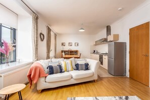 A modern living room with a sofa, a dining table, and a kitchen area with a refrigerator.