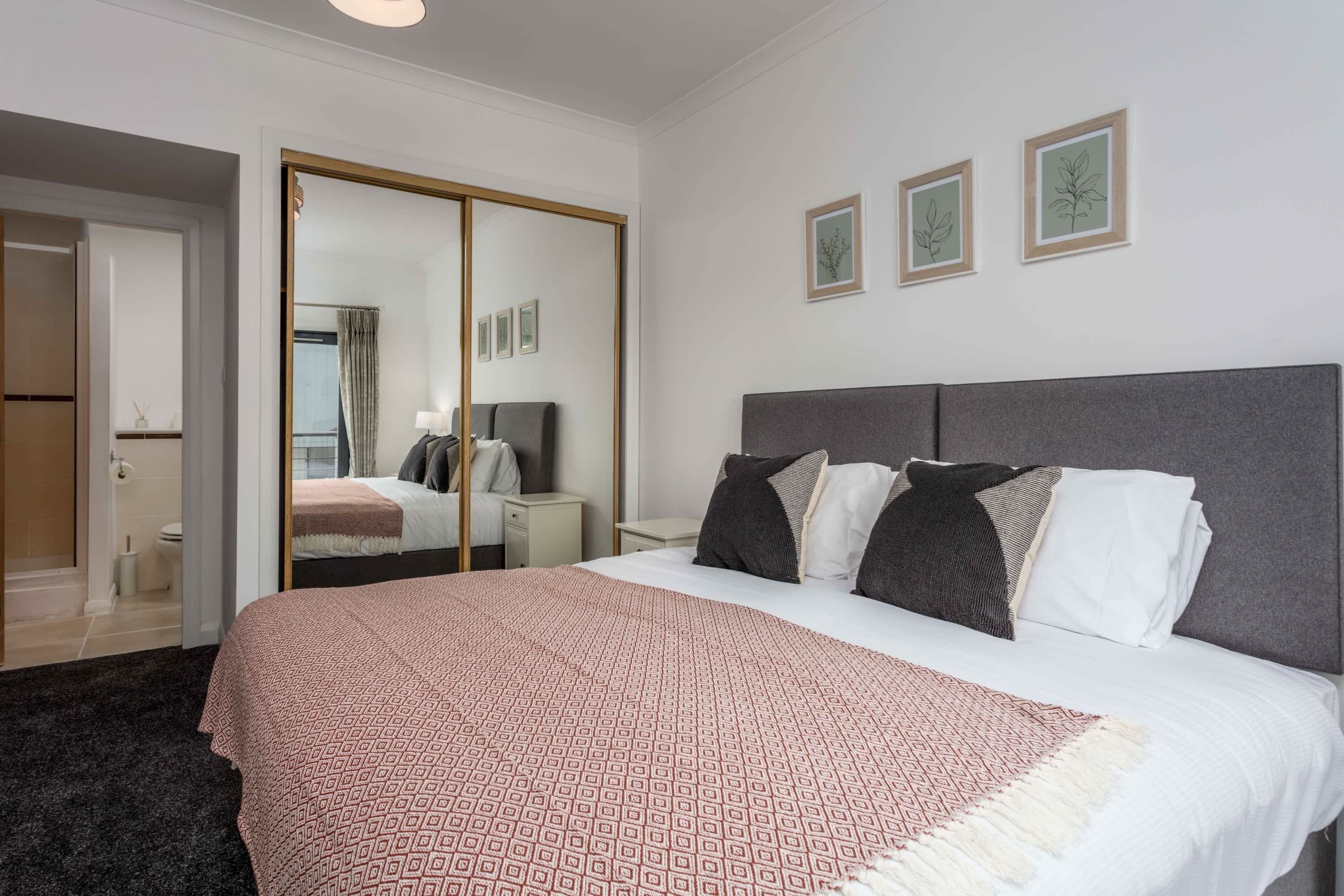 A hotel room with a large bed, a wardrobe, a mirror, and three framed pictures on the wall.
