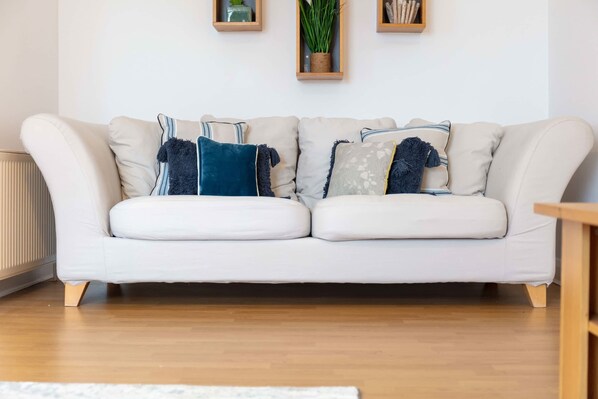 A white sofa with multiple cushions, a wooden floor, and a radiator.