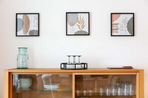 A wooden console table with glass-fronted cabinets, a teal vase, and framed abstract art on the wall. - No27 The Barclay - Donnini Apartments (Kilmarnock)