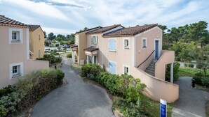 Um bairro residencial com casas de cores suaves, um caminho estreito pavimentado e vegetação exuberante.