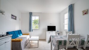 Quarto bem iluminado com cama, televisão, mesa de jantar com cadeiras e janela com cortinas.