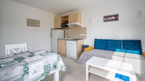 Quarto compacto com cama, cozinha compacta, mesa de jantar e uma cadeira branca.