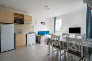 A compact living space with a kitchenette, a bed with blue bedding, a dining table with chairs, and a television.