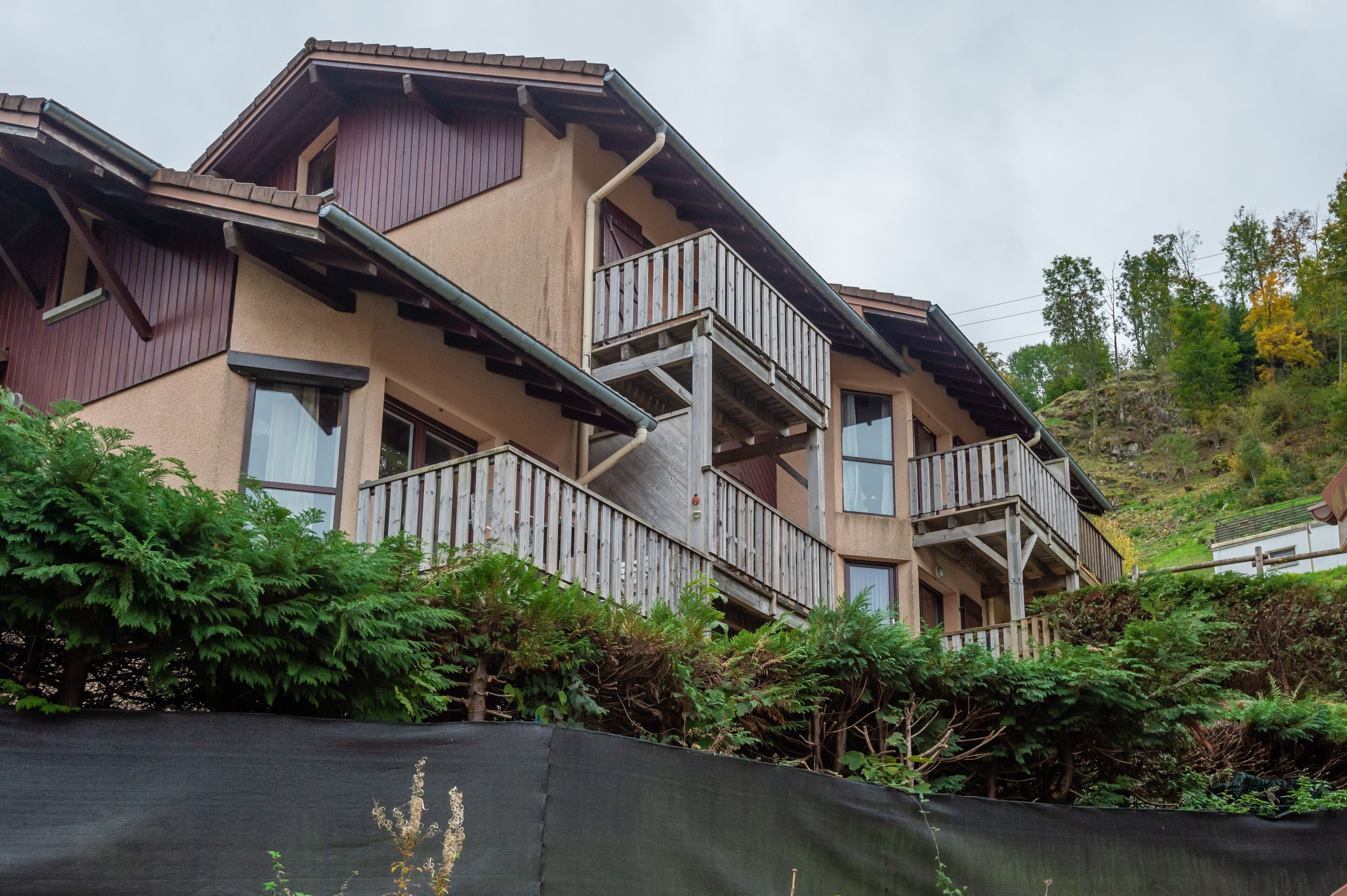 Un edificio residencial de varios pisos con techo inclinado, balcones de madera y un paisaje montañoso de fondo.