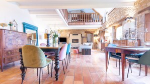 A spacious dining area with a high ceiling and exposed stone walls, featuring a wooden dining table and chairs, a fireplace, and a view of the upper level. - Kerguestenen - Longère pour 12 avec piscine (Inguiniel)