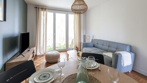 Ein modernes Wohnzimmer mit Esstisch für vier Personen, einem grauen Sofa und einem Fernseher auf einem Holzboden.