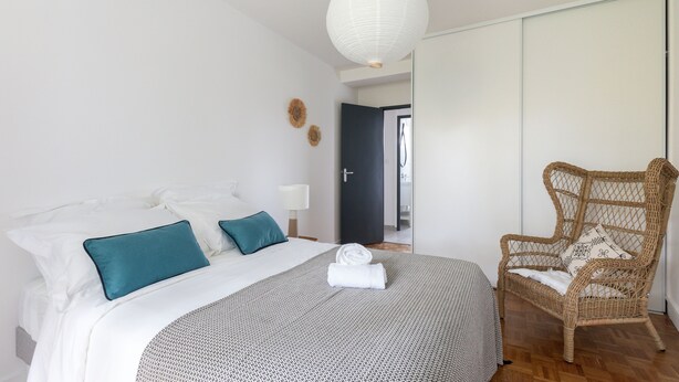 Ein Hotelzimmer mit Bett, einem Sessel, einer Hängelampe und einer Tür zu einem weiteren Raum.